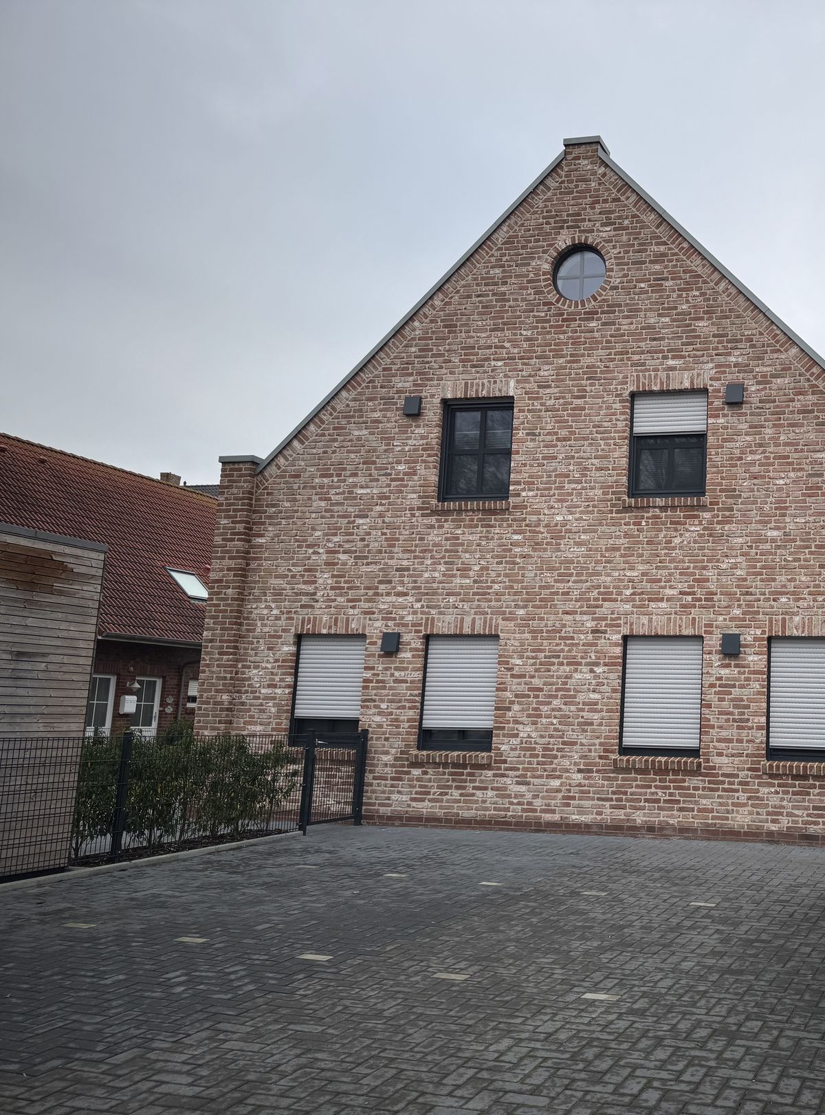 Giebelseite eines Klinkerhauses mit rundem Giebelfenster und gepflastertem Stellplatz davor